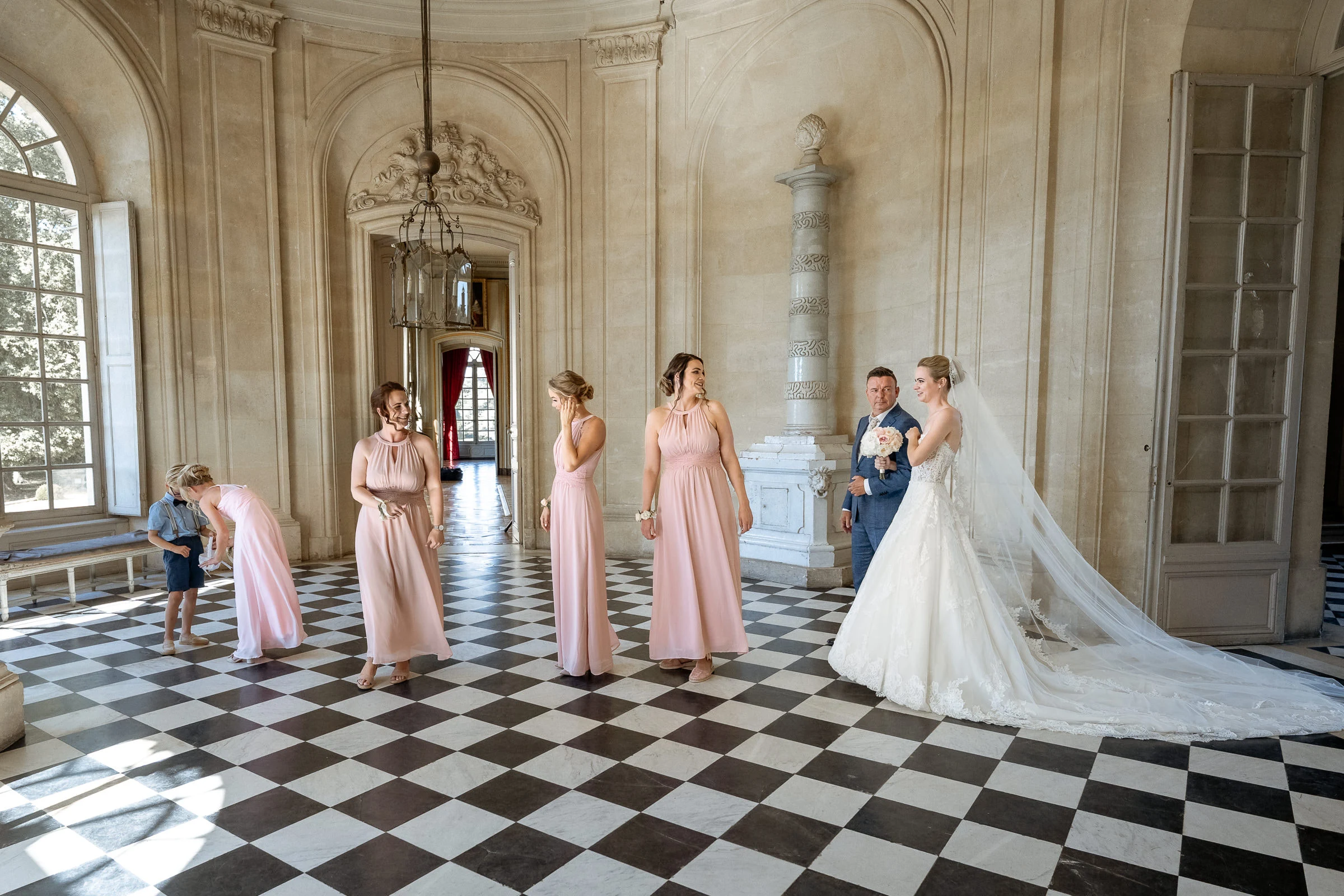 Les demoiselles d’honneur en rose et les mariés dans le vestibule au sol en damier, château de Champlâtreux