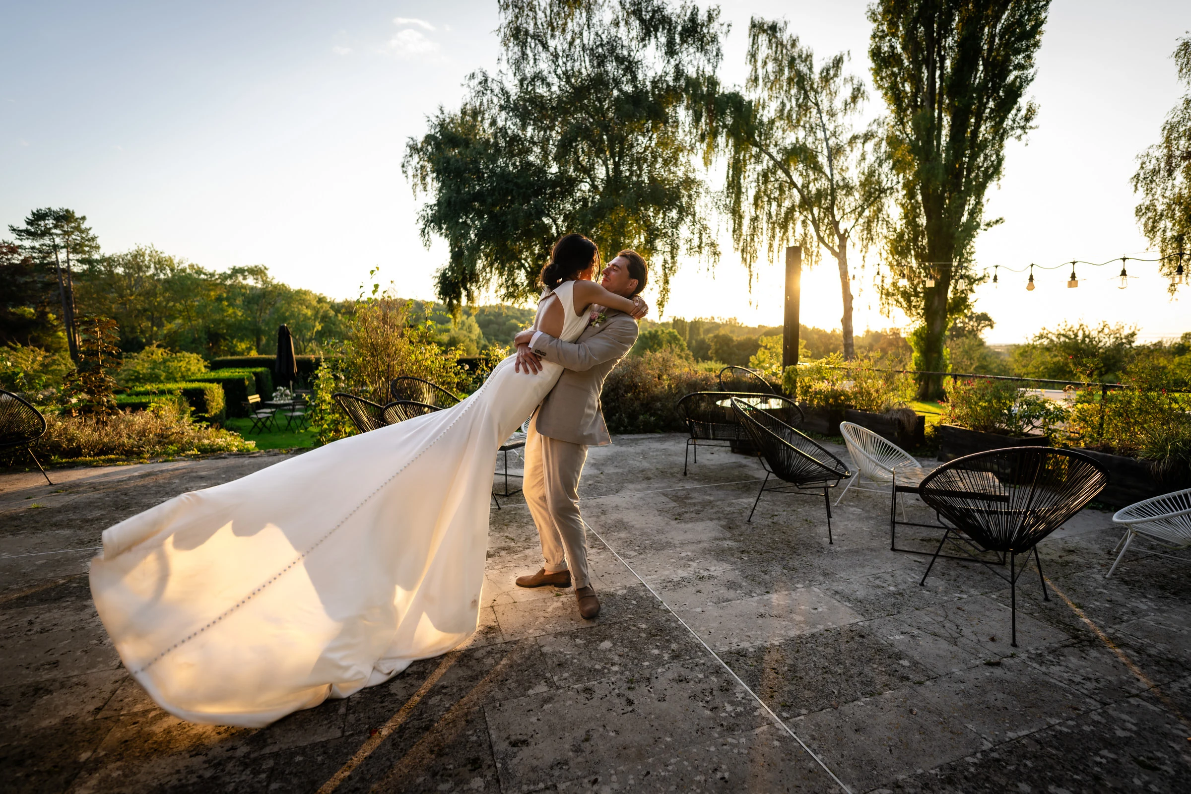 Le marié porte la mariée sur la terrasse au coucher du soleil, jardins de Coppélia près de Honfleur