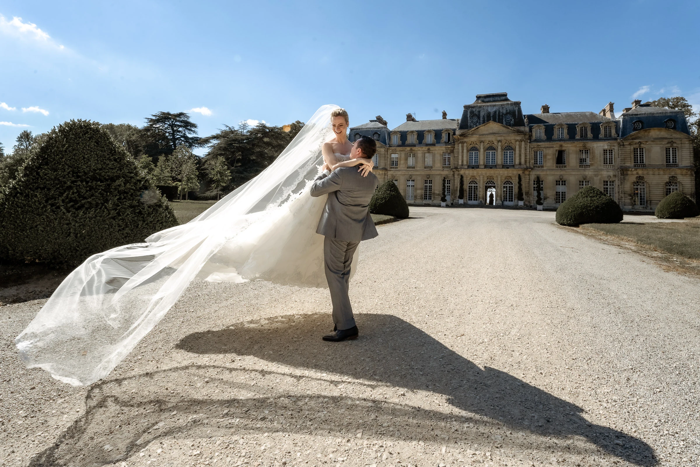 Le marié porte la mariée dans l’allée, voile emporté par le vent, château de Champlâtreux