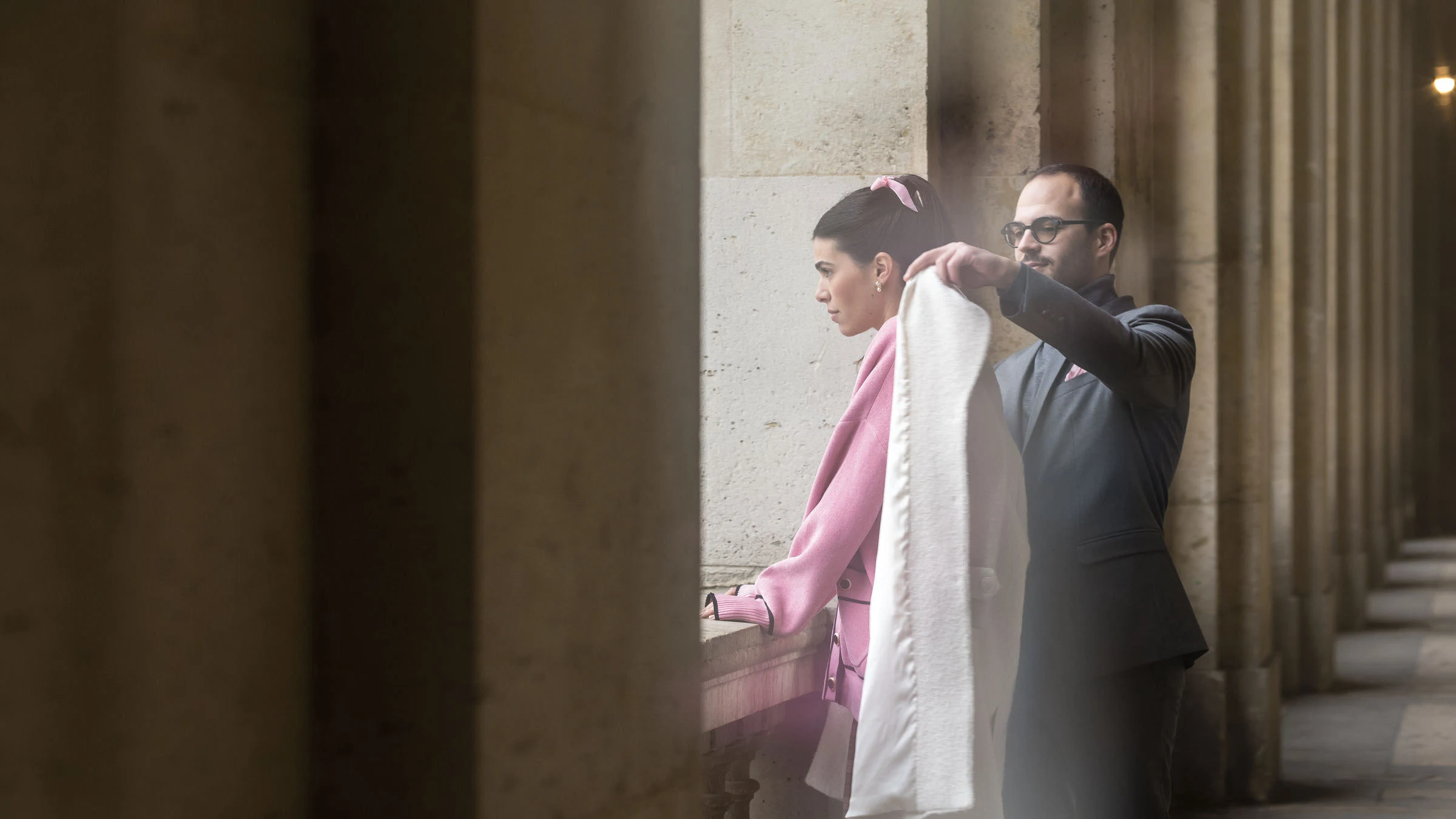Le marié pose un manteau sur les épaules de la mariée, sous les arcades