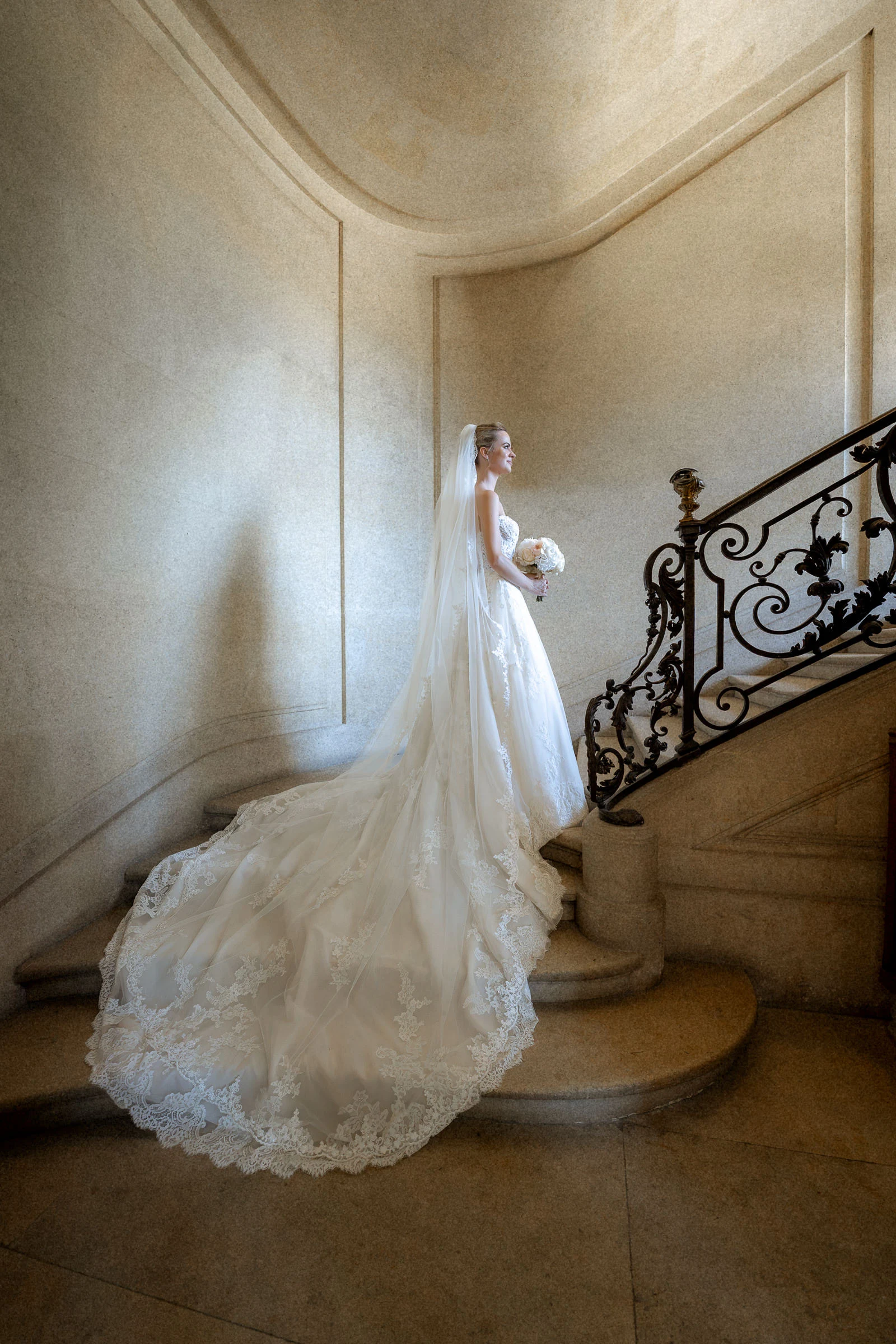 La mariée dans l’escalier de pierre à la rampe en fer forgé, château de Champlâtreux