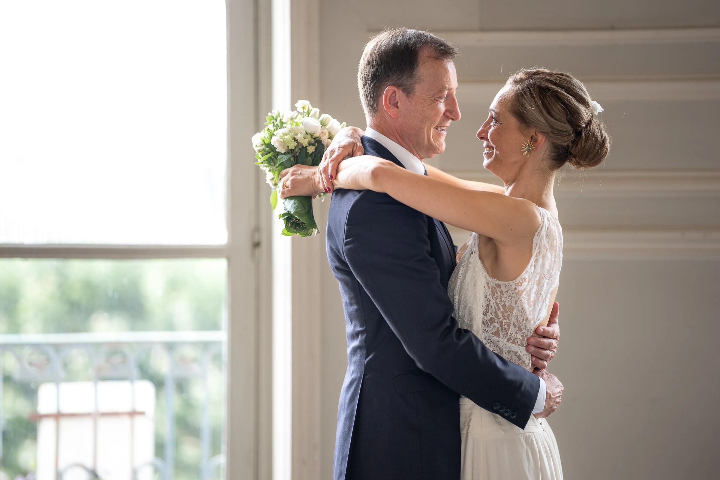 Les mariés face à face devant la fenêtre, bouquet à la main