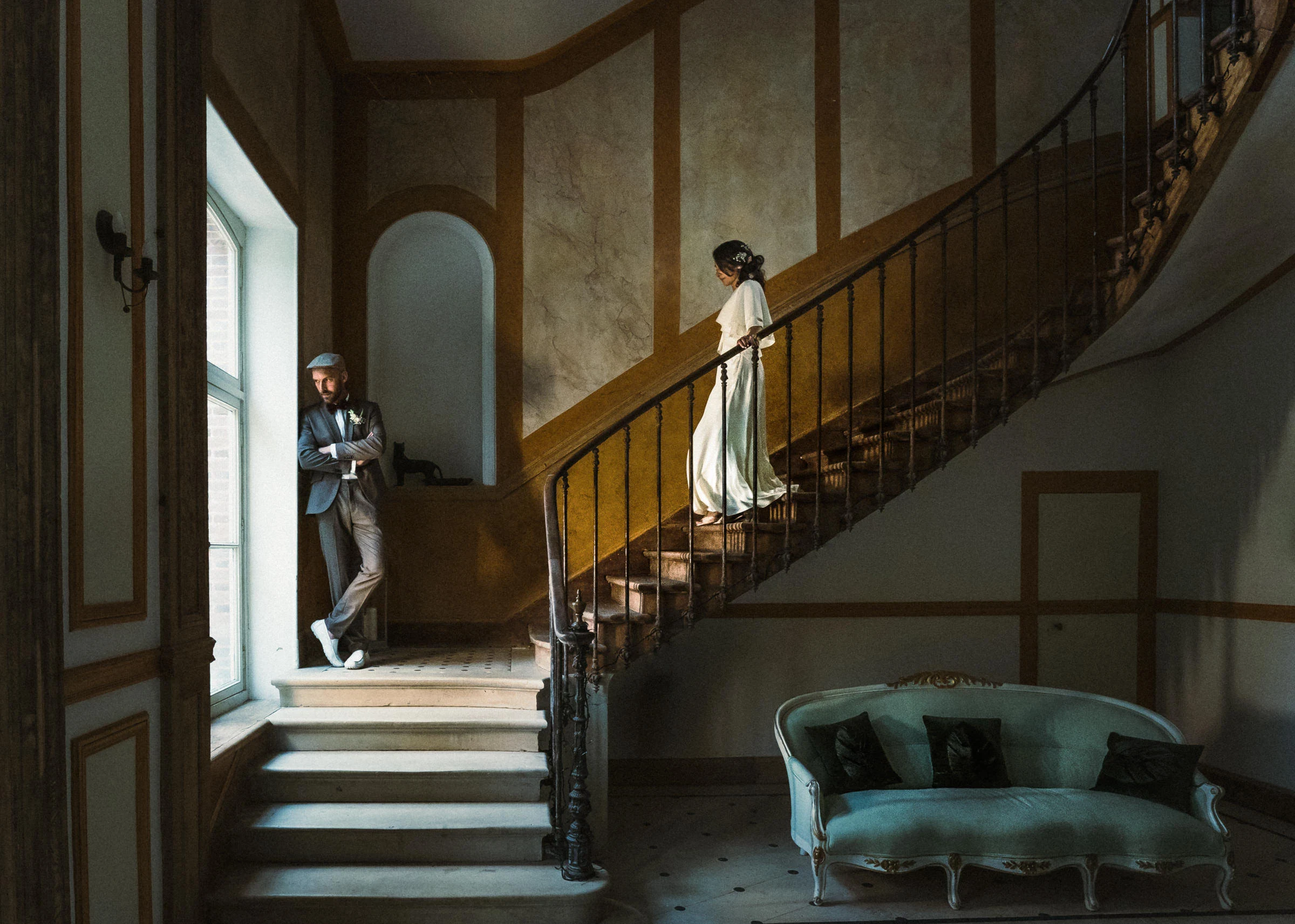The bride on the grand staircase and the groom at the window, château de la Fontaine in Griselles, Loiret
