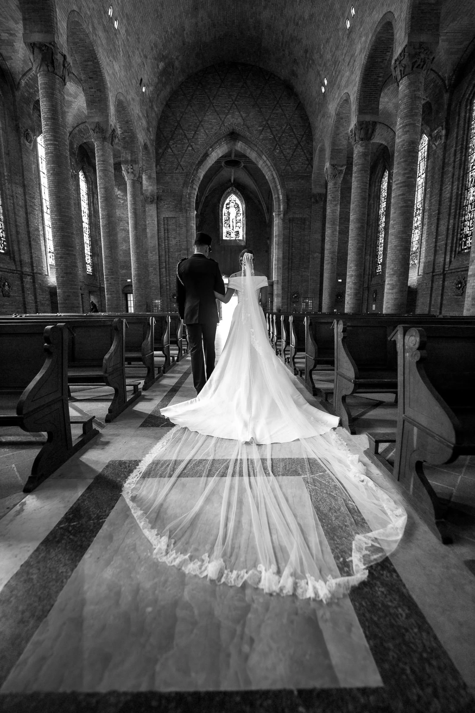The couple walking up the nave of the church of Sainte-Jeanne-d’Arc in Gien, train and veil spread, black and white