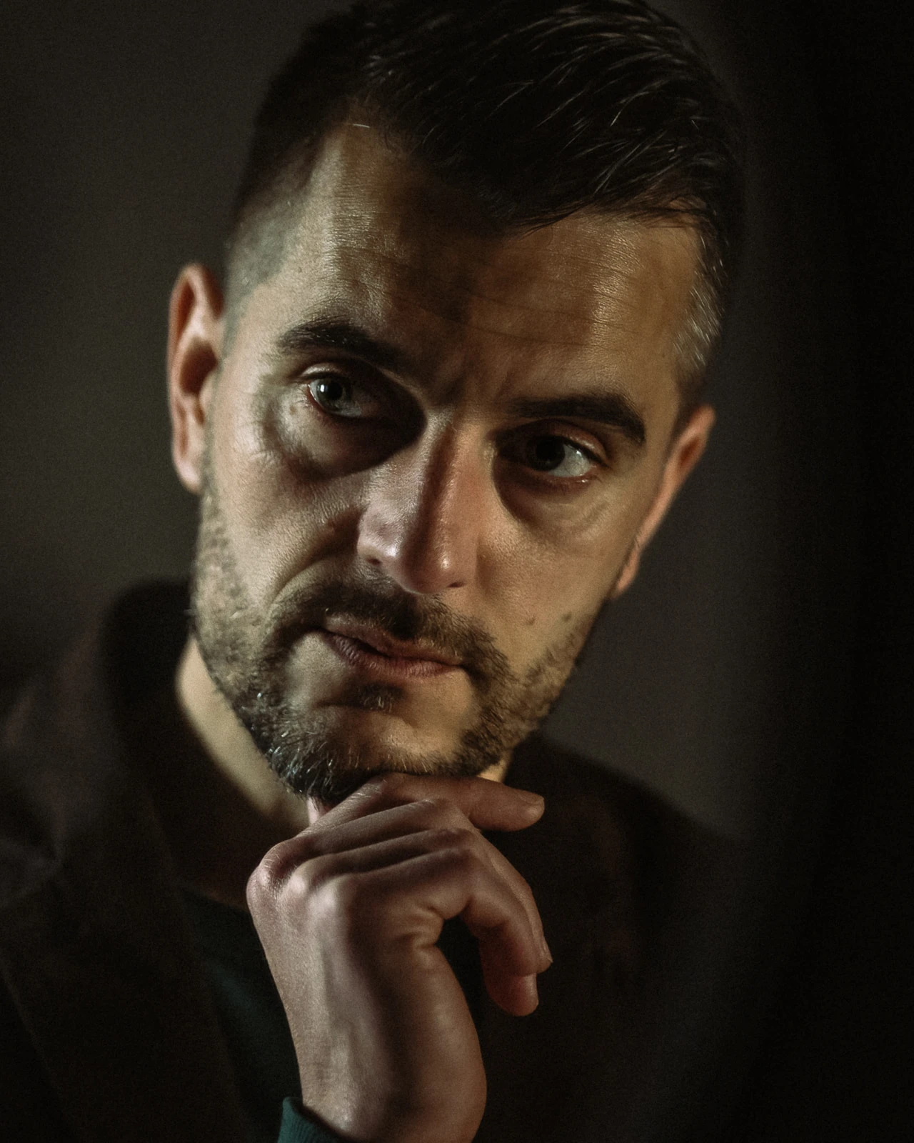 Portrait in low light, hand against the chin, eyes turned towards the light