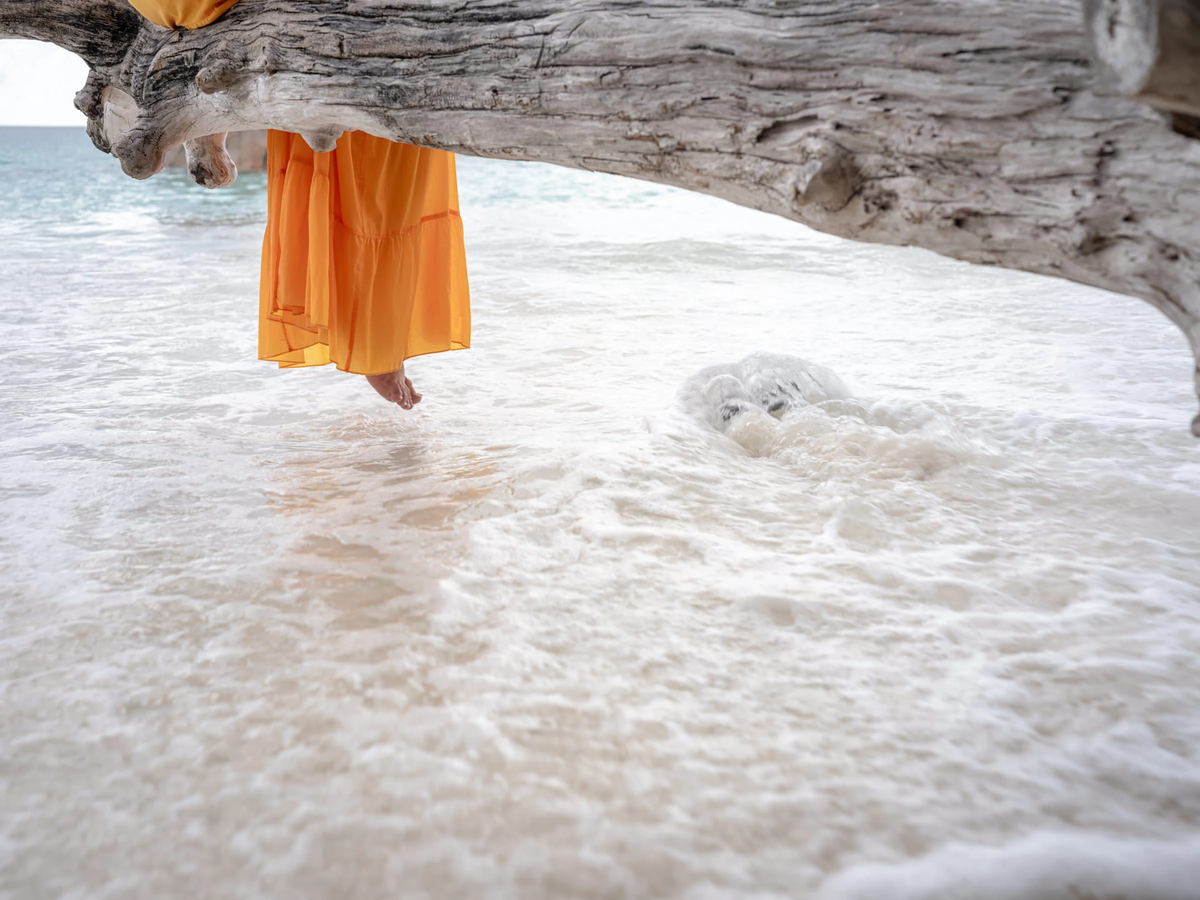 Robe orange dans l’écume sous un tronc échoué, Seychelles